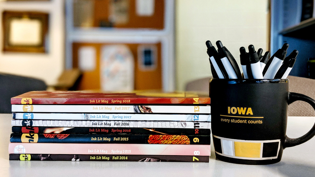 A stack of Ink Lit Mag publications next to a coffee cup full of pens.